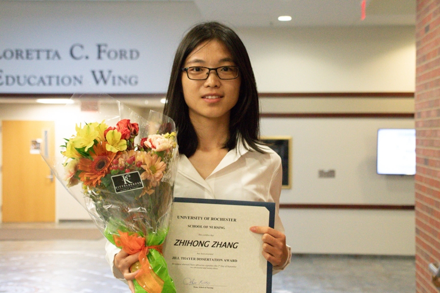 Photo of Zhihong Zhang holding her award certificate and a bouquet of flowers.