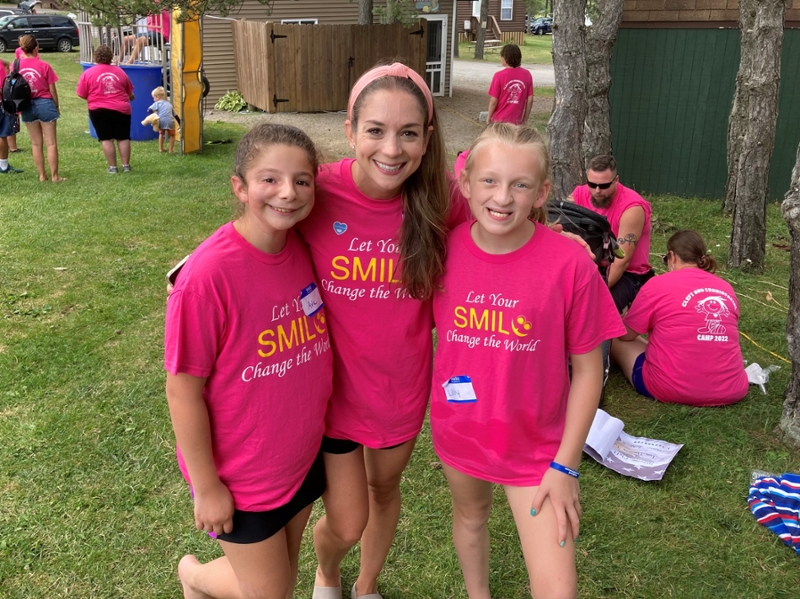 Mel Ploutz and two summer camp participants wear matching pink shirts with the quote "Let your smile change the world" in yellow letters.