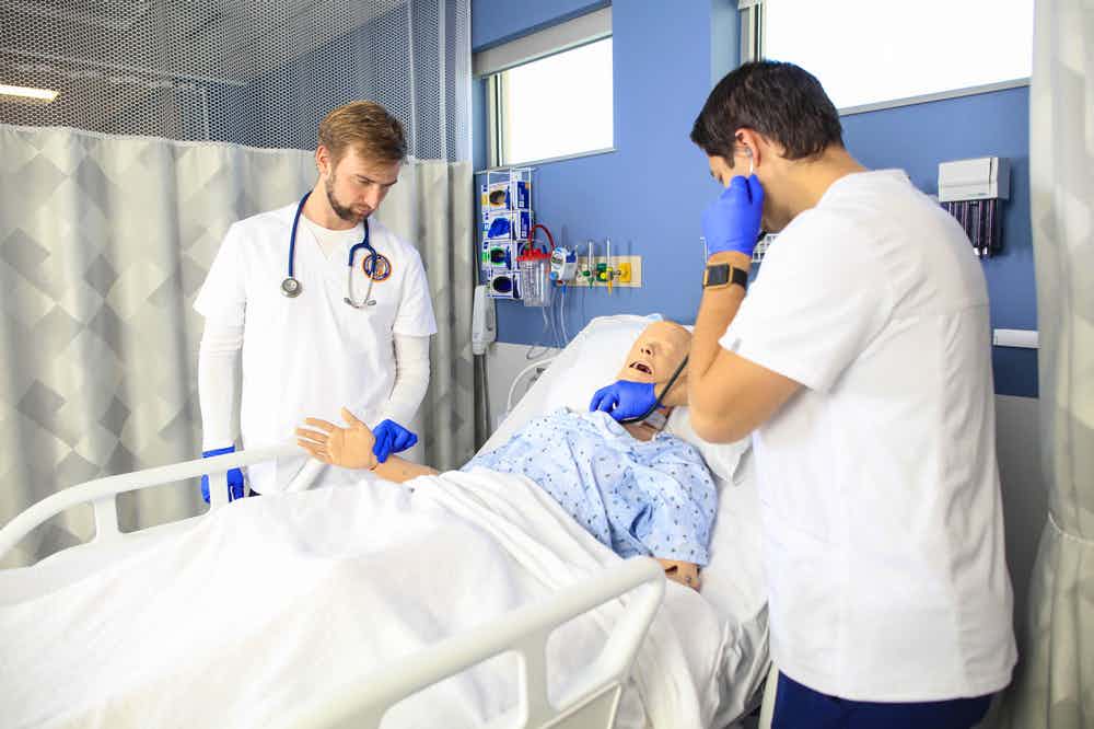 Two ABSN students in nursing uniform looking at manikin.