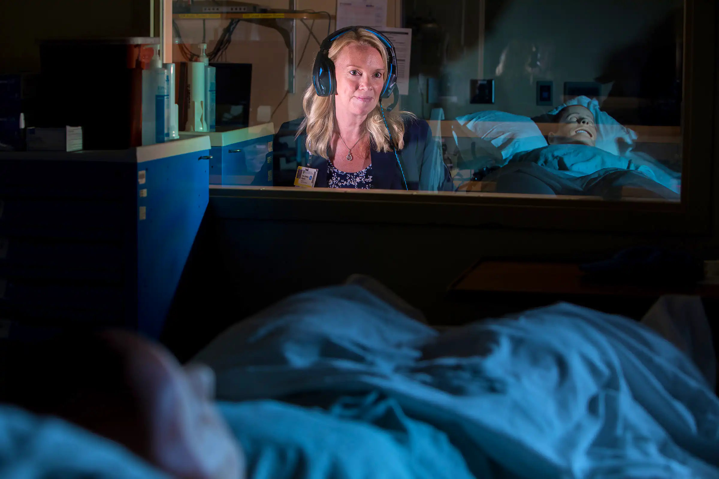 Erin Baylor in control room window with simulation mannequin