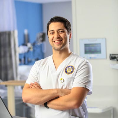 Joshua Billings in the School of Nursing skills lab, in a white uniform.