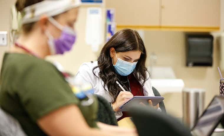 Nurse with mask on looking at iPad in clinical setting