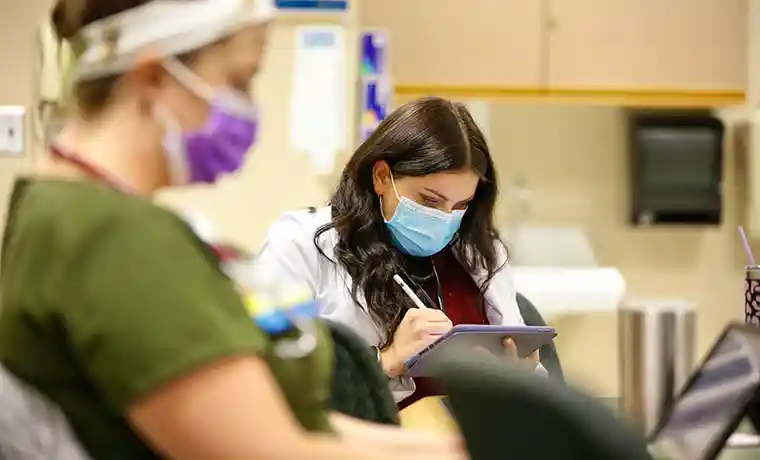 Nurse with mask on looking at iPad in clinical setting