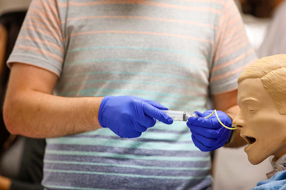 Gloved hands inserting IV in simulation man.