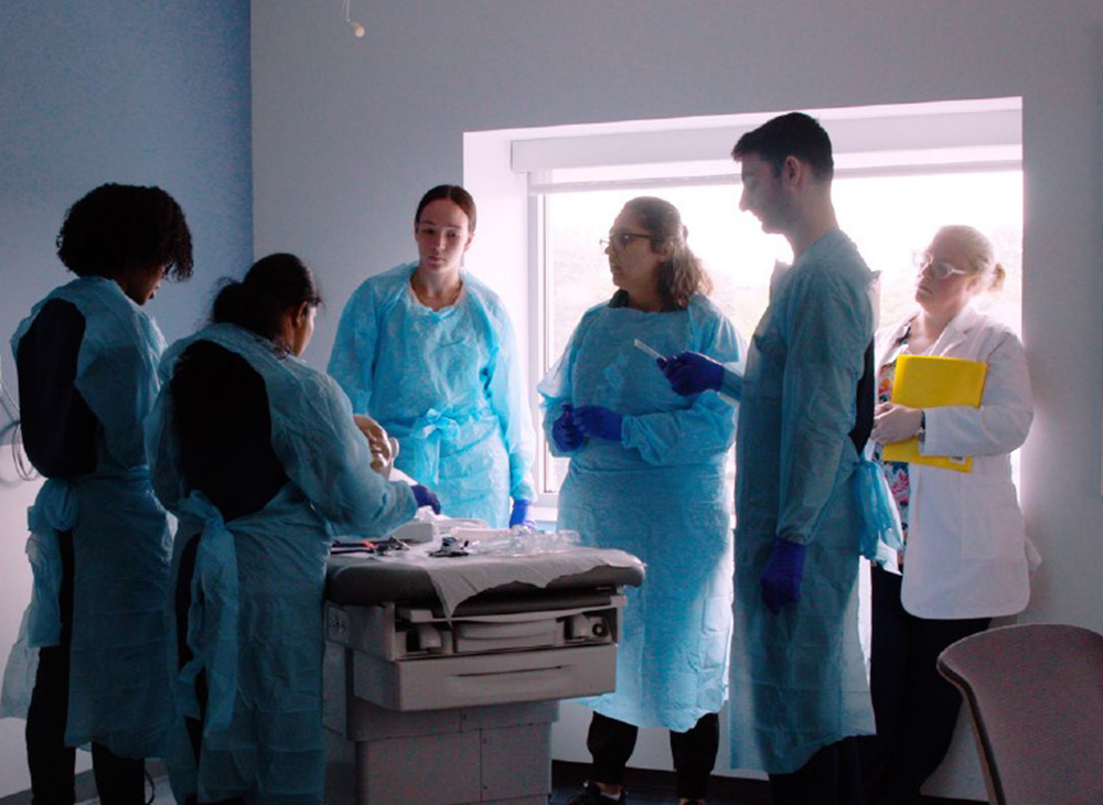 Group of nursing students around a patient bed using a skill trainer.