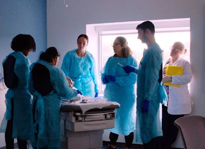 Group of nursing students around a patient bed using a skill trainer.