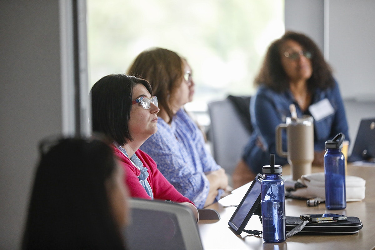 A group of women seated at a conference table attentively listening to a presentation