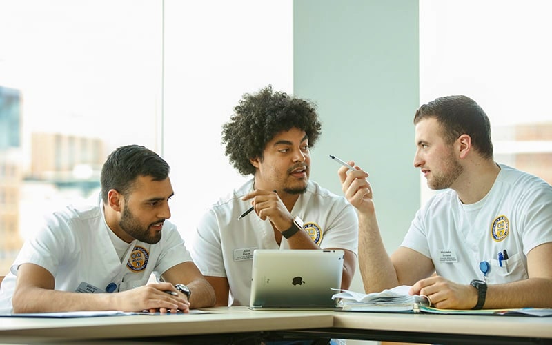 Three male nursing students at a desk talking to one another with iPads