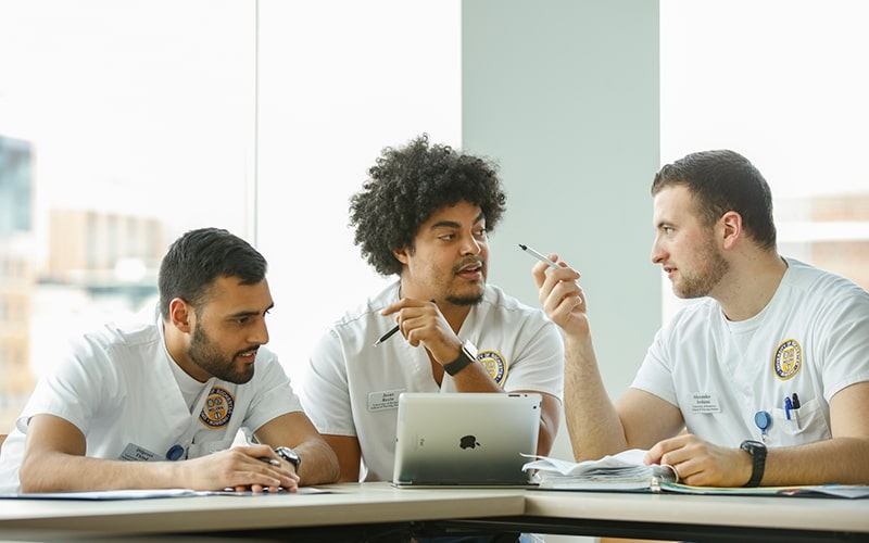 Three male nursing students at a desk talking to one another with iPads