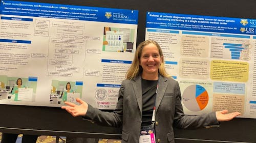 Meghan Underhill-Blazey poses with two conference posters about her research in cancer genetics.