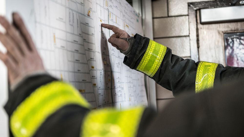 View of firefighters' arms in black and neon yellow uniforms as they look at a map.