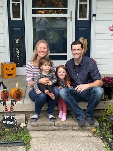 Family photo of Melissa, her husband and two daughters on a front porch, surrounded by Halloween decoratins.