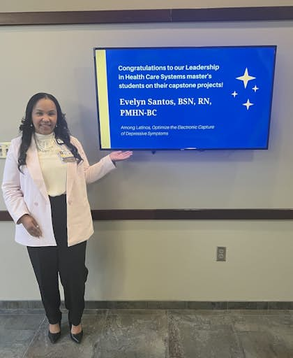 Evelyn Santos poses with a TV screen display congratulating her on her capstone project.