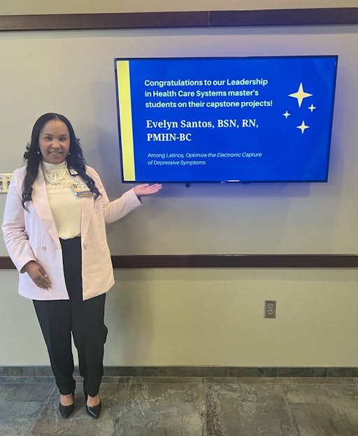 Evelyn Santos poses with a TV screen display congratulating her on her capstone project.