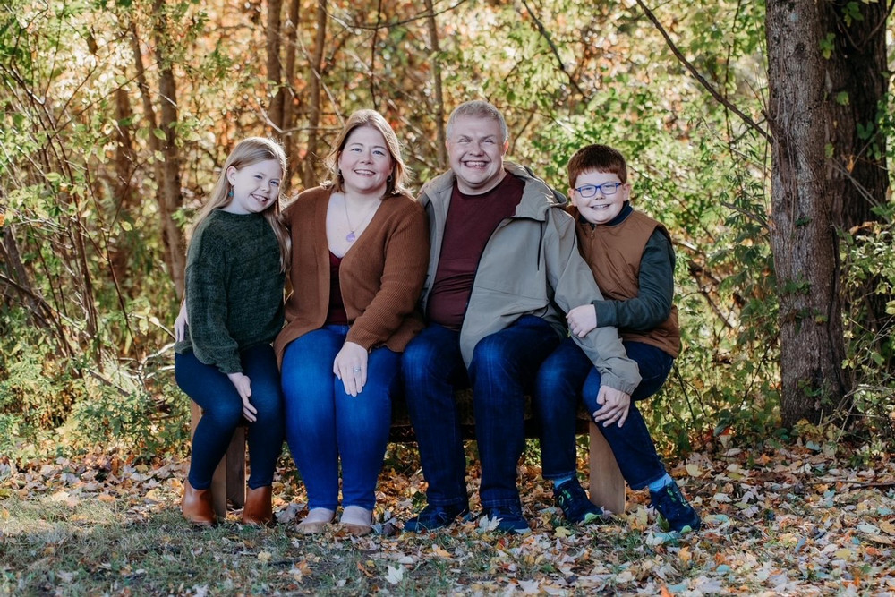 Adrianne Edlund, her husband and children sitting for a family photo on a bench with trees behind them.