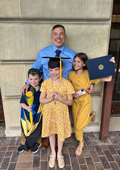 Joseph Escobar takes a graduation photo with his 3 children, who are holding his cap, stole, and diploma