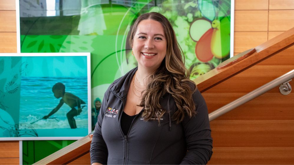 Photo of Amanda Welter on a staircase in the Children's Hospital, with a bright blue and green mural behind her.