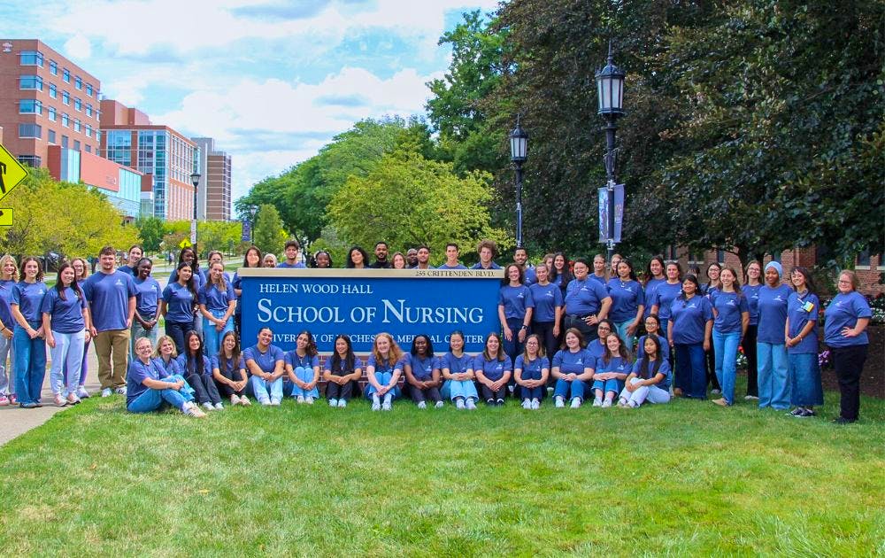Group photo of students in matching blue shirts on the lawn of School of Nursing