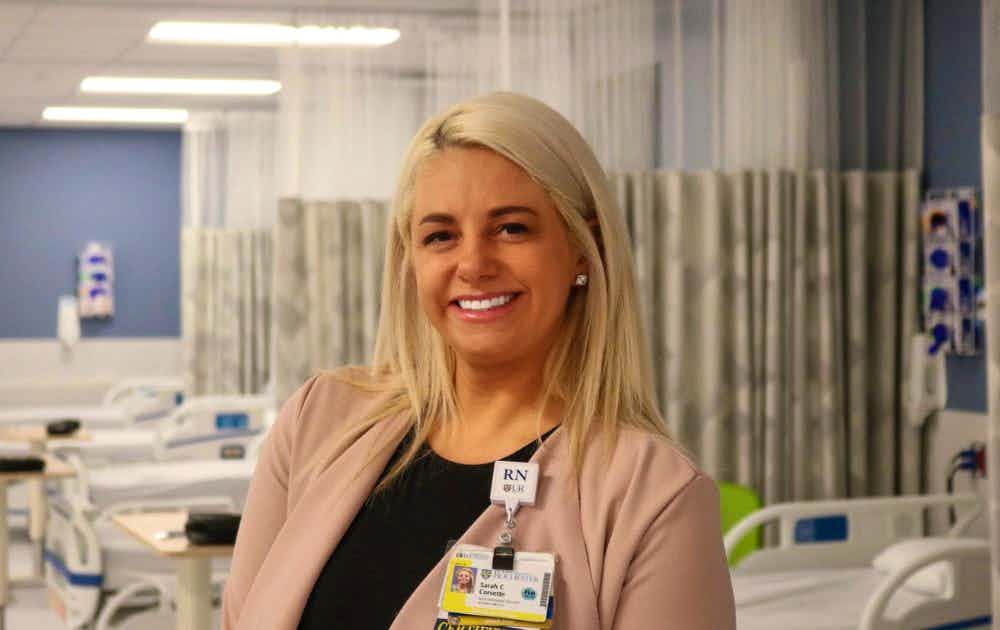 Photo of Sarah standing in a clinical skills lab, a row of empty patient beds behind her.
