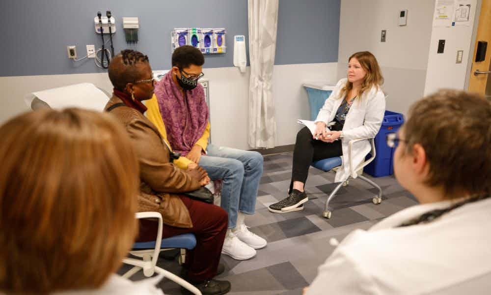 NP student talks to two standardized patient actors in an experiential learning classroom, designed to simulate a patient room.