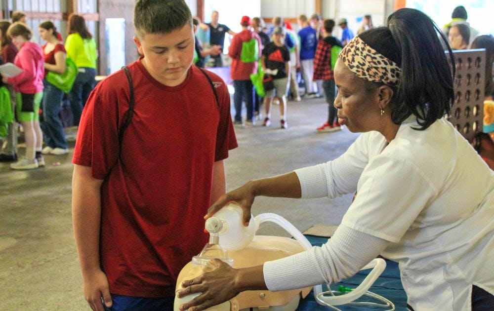 A nursing student shows a middle schooler how to do CPR on a dummy. 