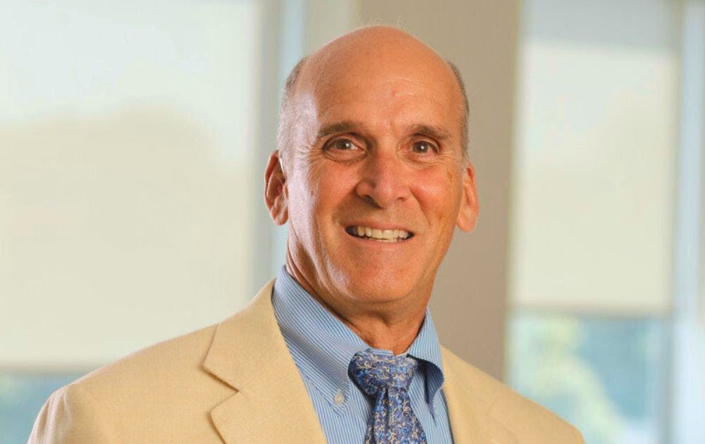 Jeff Houck's headshot; he is wearing a white suit jacket and light blue shirt and tie