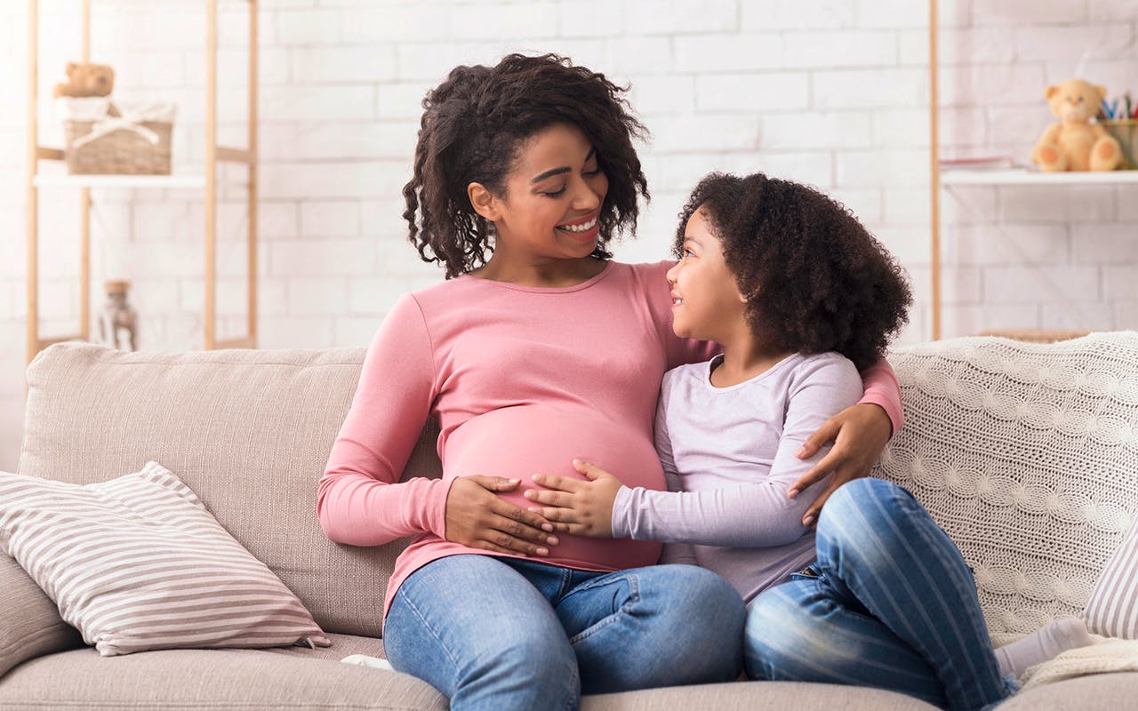 Pregnant woman and her young daughter smiling and holding their hands on her pregnant belly