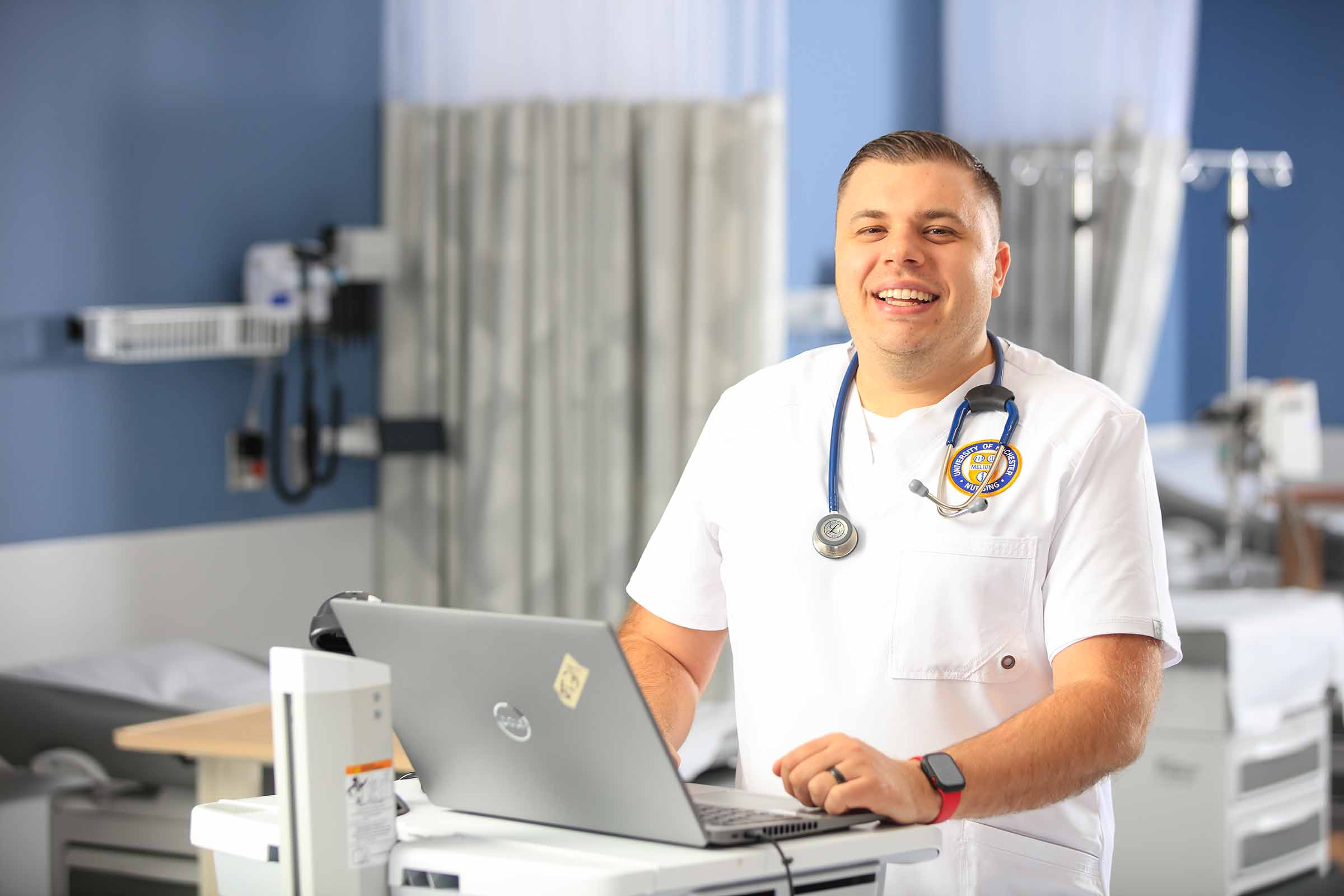Cam Dove, nursing student, in white and blue nursing uniform, smiling at a camera