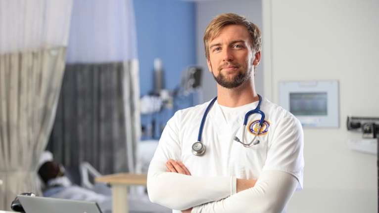 Tom Ruffing, in white and blue nursing uniform, smiling at a camera